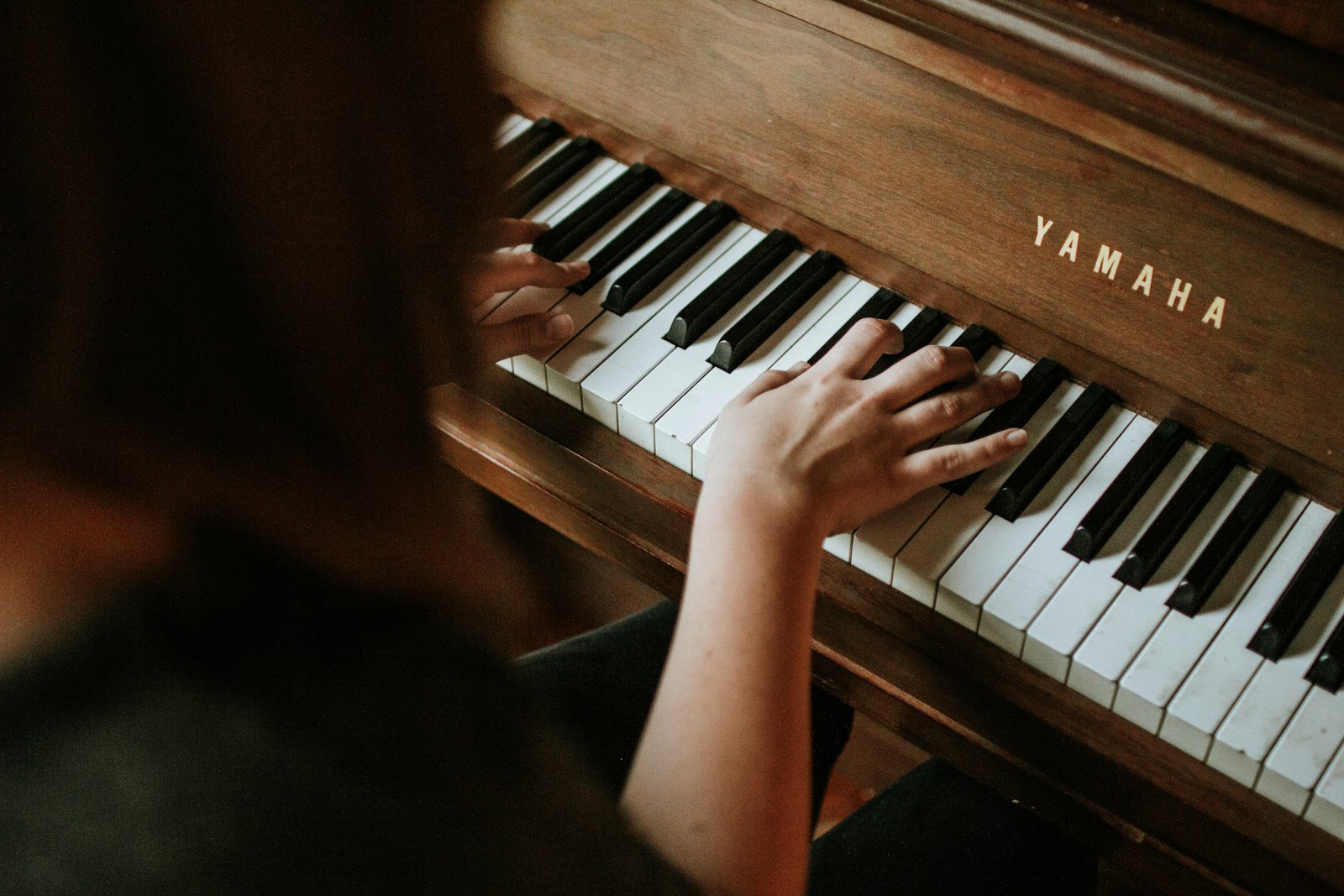 Hands at a warm wooden upright piano keyboard